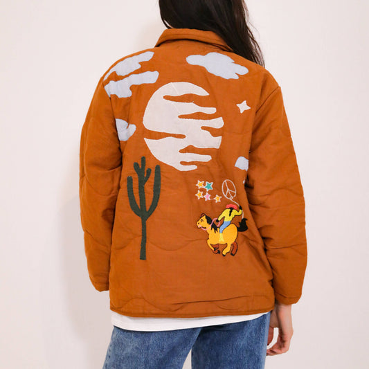 Quiltad jacka med westernmönster med broderad cowboy, häst, kaktusar och moln.
Allt gjort i en cool lappteknik. Här har du en nättare jacka med skjortkrage, knäppning och två fickor. Vi älskar den!
