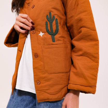 Quiltad jacka med westernmönster med broderad cowboy, häst, kaktusar och moln.
Allt gjort i en cool lappteknik. Här har du en nättare jacka med skjortkrage, knäppning och två fickor. Vi älskar den!